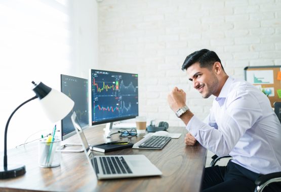 Attractive Freelance Stock Trader Celebrating Profit Share Confident handsome Hispanic financial broker showing fist to computer screen while trading from home